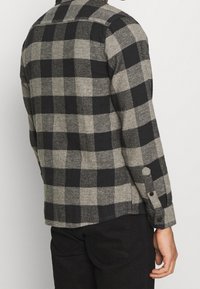 Schwarz-grau kariertes Flanellhemd mit Button-Down-Kragen, langen Ärmeln und schwarzen Knöpfen mit weicher, strukturierter Oberfläche.