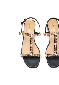 Sandalia negra con diseño de tira en T, que presenta piedras decorativas de varios colores a lo largo de las tiras y una textura de cuero suave.