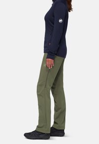 Haut à manches longues bleu marine avec logo sur le bras, associé à un pantalon élastique vert olive avec des zips sur les côtés, complété par des baskets noires.