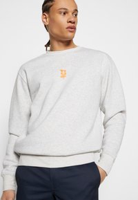 Light gray sweatshirt made from soft fabric, featuring long sleeves and an orange logo on the chest and back. Relaxed fit with ribbed cuffs.