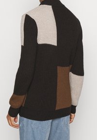 Stickad tröja med en färgblockdesign i svart, beige och brunt. Texturerat tyg med hög krage och ribbade ärmslut.