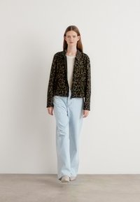 Zwarte en groene panterprintjas met een rits aan de voorkant, gecombineerd met lichtblauwe wijde jeans. Gladde textuur, moderne cropped stijl.