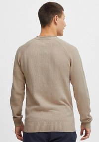 Beige strikket sweater med ribbede kanter og manchetter, der har en klassisk rund hals og raglanærmer, og som viser en glat tekstureret finish.