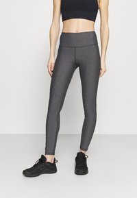 Grå högmidjade leggings med slät textur, med en åtsittande design och subtila sömnadsdetaljer. Kombinerat med svarta träningsskor.