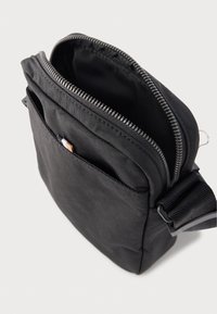 Schwarze Umhängetasche aus strapazierfähigem Stoff mit einem Reißverschluss-Hauptfach und einer Fronttasche. Glatte Textur mit verstärkten Nähten.