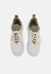 Scarpe da ginnastica di un beige chiaro con una parte superiore liscia in materiale sintetico, accentuate da dettagli beige scuri e lacci color crema. Suola in gomma bianca.