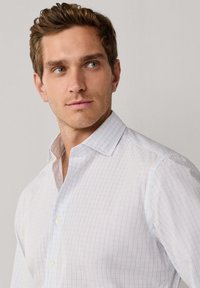 Witte blouse met een licht ruitpatroon in blauw en beige. Bevat een gespreide kraag en een gestructureerde stof.