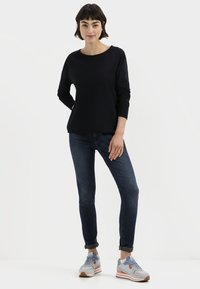 Zwarte lange mouwen top met ronde hals, gecombineerd met donkerblauwe skinny jeans en grijze sneakers met oranje accenten. Eenvoudige, casual outfit.