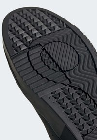 Suola di scarpa in gomma nera con motivi testurizzati. Caratterizzata da un'area di presa circolare e diversi design del battistrada per trazione e stabilità.