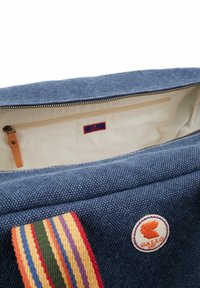 Blue canvas bag with a zippered top, featuring a striped shoulder strap and an embroidered logo. Cream interior with a zip pocket.