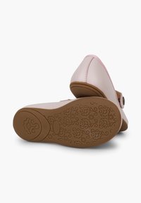 Zapatos de color rosa claro con un upper liso, correa ajustable y suela de goma marrón texturizada con patrones florales.