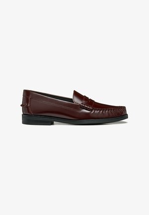 Mocassino in pelle marrone scuro con tacco basso nero e cuciture stile mocassino sulla parte frontale e sui lati su sfondo bianco.