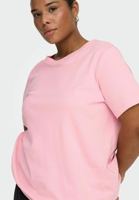 Różowy bawełniany t-shirt o luźnym kroju, z okrągłym dekoltem i krótkimi rękawami. Materiał wydaje się gładki i miękki, odpowiedni do noszenia na co dzień.