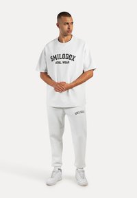 Weißes Sport-Outfit bestehend aus einem kurzärmeligen Oberteil mit einem Logo und passenden Sweatpants, beide aus weichem Stoff mit einer lockeren Passform.