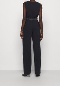 Meripuku, jossa on istuva yläosa ja leveät lahkeet. Varustettu ruutukuosisella vyöllä ja huomaamattomalla takavetoketjulla. Sileä pinta, räätälöity muotoilu.