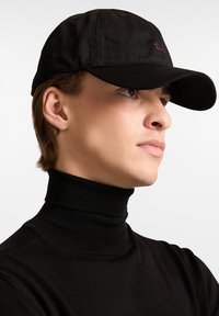 Svart basebollkeps med en böjd skärm, prydd med en liten lila broderad design. Kepsen är tillverkad av ett slätt tyg.