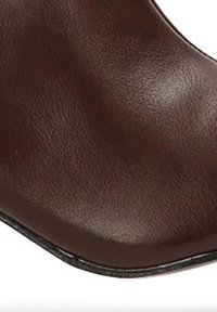 Zapato de cuero marrón oscuro con punta redonda y suela negra, mostrando una textura suave y un leve brillo.