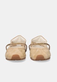 Zapatos planos de ante beige con punteras redondeadas y una sola correa decorada con tachuelas doradas en el frente.