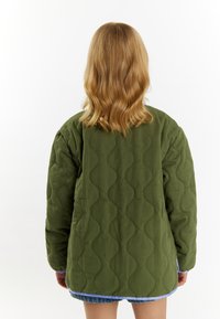 Quiltet grøn jakke med en bølgende tekstur, der har en blå kant langs kanten. Designet er oversized med sænkede skuldre.