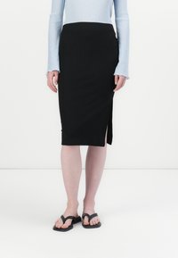 Jupe midi noire à côtes avec fente sur le côté, assortie à un haut à manches longues bleu clair et des tongs noires. Silhouette simple et ajustée.