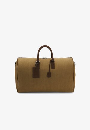 Brun duffelbag i lærred med læderhåndtag, lynlåslukning og fastgjort læderbagagemærke på en hvid baggrund.