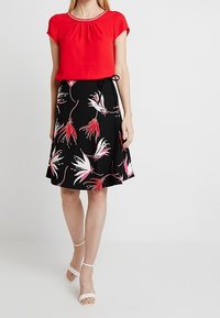 Top rosso a maniche corte con scollatura rotonda, abbinato a una gonna nera con stampa floreale rosa e bianca e dettaglio in vita legato.