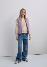 Veste matelassée lavande sur un pull crème avec motif crâne, jean large taille haute bleu, et baskets à motifs avec semelles claires.