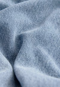 Gros plan sur un tissu en denim bleu clair montrant la texture et le tissage avec des plis doux et des ombres.