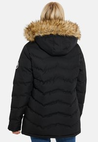 Zwarte pufferjack met een capuchon en nepbontafwerking, met een doorgestikt ontwerp en geribde manchetten. Gekocht met blauwe jeans.