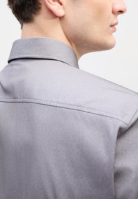 Sivá košeľa s golierom a hladkou textúrou, so zjavnou švom pozdĺž chrbta a štruktúrovaným golierom.