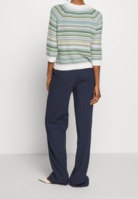 Gestreepte gebreide trui met korte mouwen in groen, blauw en geel op een witte achtergrond; gecombineerd met marineblauwe wijde broek.