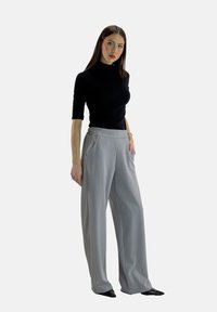 Maglione nero con collo alto abbinato a pantaloni larghi grigi chiari con tasche laterali e una texture liscia. Indossati con ballerine nere a punta.