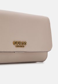 Portafoglio in ecopelle beige chiaro con il logo dorato "GUESS" e il dettaglio "EST 1981". Caratterizzato da una texture pulita e liscia e bordi cuciti.