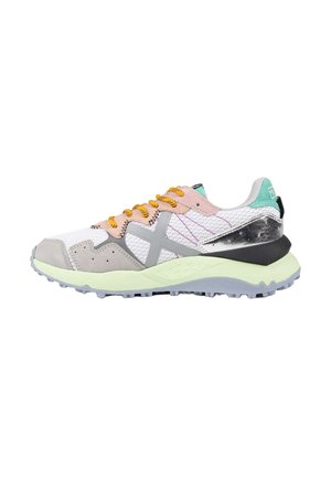Zapatilla blanca con detalles en gris, rosa, verde y negro, cordones amarillos, parte superior de malla y suela texturizada, mostrada de lado sobre fondo blanco.