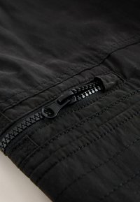 Gros plan sur une fermeture éclair en tissu noir sur un matériau matelassé, montrant le curseur de la fermeture éclair et les coutures détaillées.