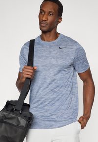 Αθλητική μπλούζα σε ανοιχτό γαλάζιο με ελαφρώς ραβδωτή υφή, στρογγυλή λαιμόκοψη και κοντά μανίκια. Φέρει μαύρο λογότυπο Nike στο στήθος.