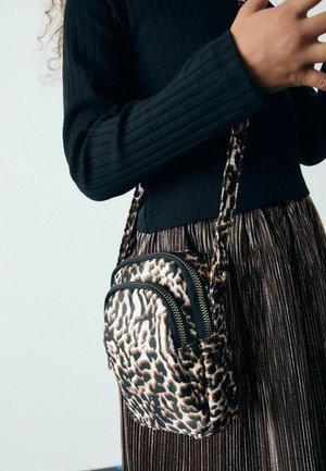 Torba s motivom leopardovih pik v obliki crossbody, z dvema zapiranima predeloma, črnimi detajli in tankim nastavljivim trakom. Vidni so črn riban zgornji del in metalna krila.