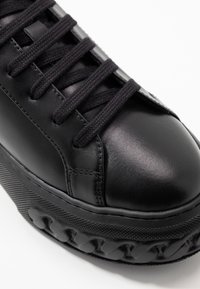 Baskets en cuir noir avec semelle en caoutchouc texturé, lacets plats noirs et bout arrondi. Présente un design épuré et des détails de couture subtils.