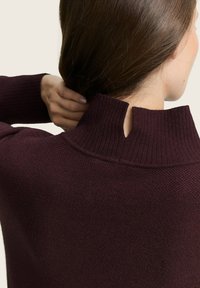 Burgunderfarbener Strickpullover mit hohem geripptem Kragen und einem kleinen Ausschnitt auf der Rückseite, ausgestattet mit einem strukturierten Stoff in einer taillierten Passform.