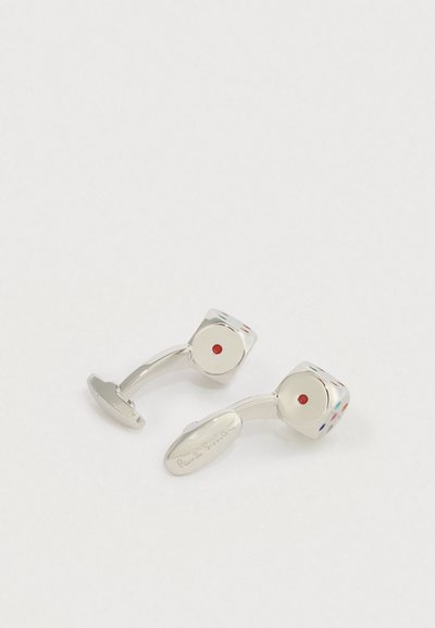 Gemelos plateados en forma de dados con puntos de colores, uno con la inscripción "Paul Smith" en la parte trasera.