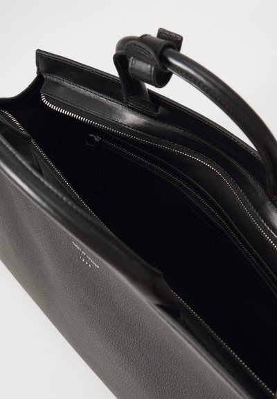 Schwarze Leder-Tote-Bag mit strukturierter Oberfläche, ausgestattet mit einem Reißverschluss und mehreren Innentaschen. Robuste Tragegriffe zum Transport.