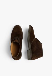 Botas de tobillo de ante marrón con puntera redonda, diseño de cordones y suelas de goma texturizadas. El forro interior suave complementa el diseño general.