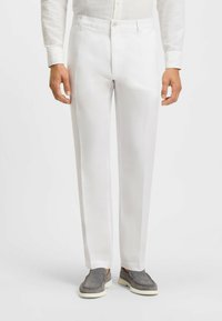 White, tailored trousers with a smooth texture, featuring a zip fly and side pockets, paired with gray slip-on shoes.