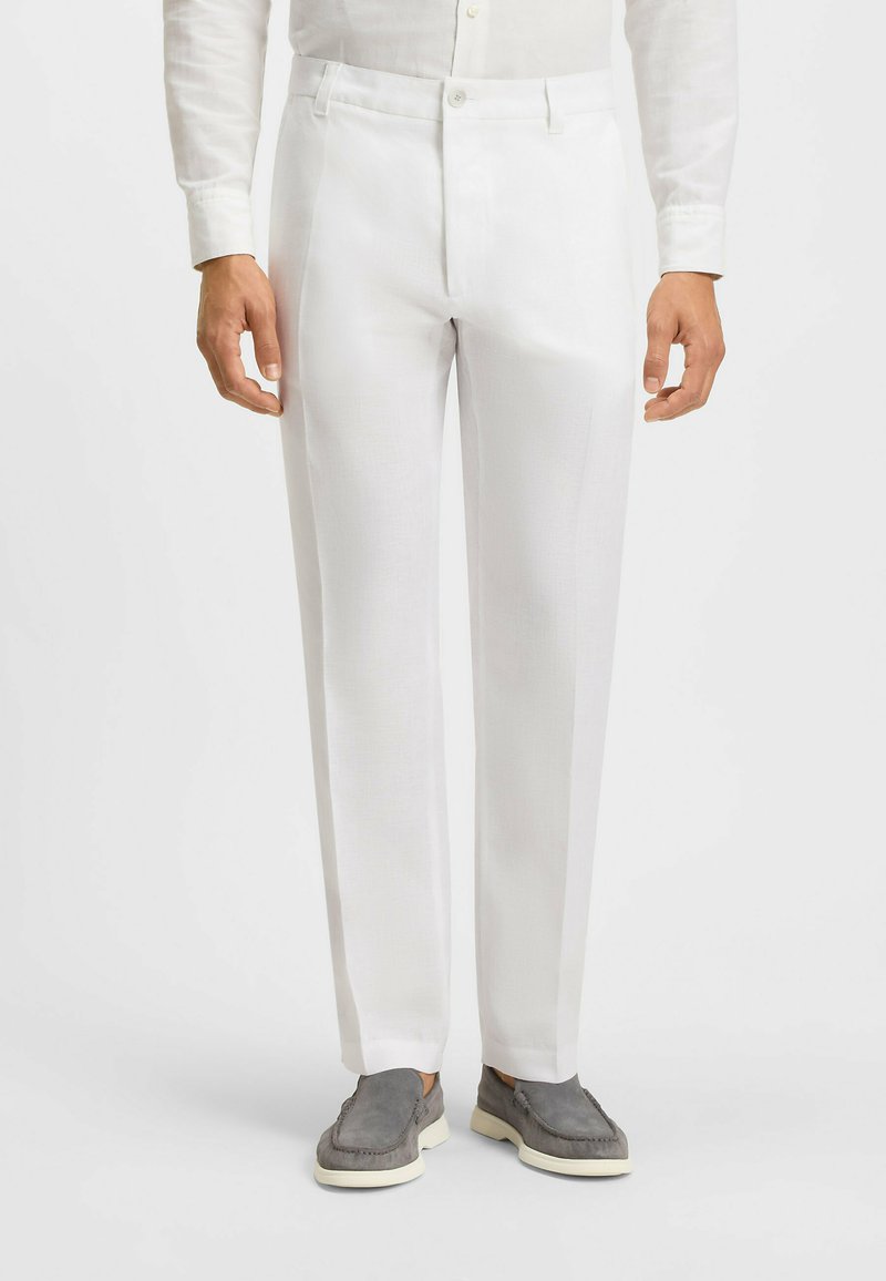 White, tailored trousers with a smooth texture, featuring a zip fly and side pockets, paired with gray slip-on shoes.