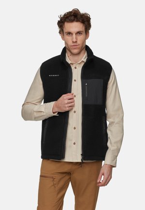 Black fleece vest with high collar, zippered front pockets, and a chest pocket. Features textured fabric and a logo on the front.