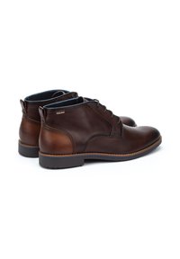 Botas de tobillo de cuero marrón con un acabado suave, diseño de cordones, cuello acolchado y detalles en contraste en color beige en el talón y el costado.