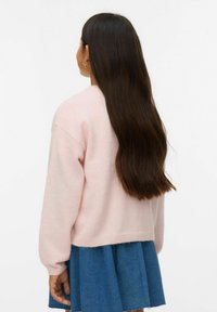 Šviesiai rožinis, tekstūruotas megztinis su ilgomis rankovėmis, derinamas su mėlyna džinsine sijonu. Megztinis laisvo silueto, su ribbintais kraštais apačioje.