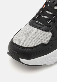 Černé a šedé tenisky s síťovanou tkaninou a koženými akcenty. Mají texturovaný, detailní svršek, ploché černé šňůrky a bílou podrážku.