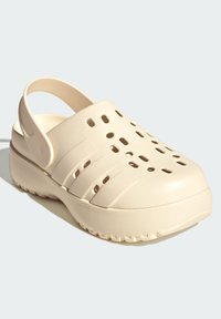 Sabot en plastique beige avec plusieurs trous d'aération, un bout arrondi et une lanière à l'arrière pour le soutien. Semelle texturée pour la traction et la stabilité.