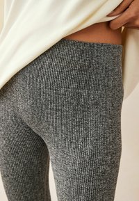Grå rippade leggings med en texturerad stickad design och hög midja. Tyget verkar mjukt med en subtil glans som förstärker den övergripande looken.
